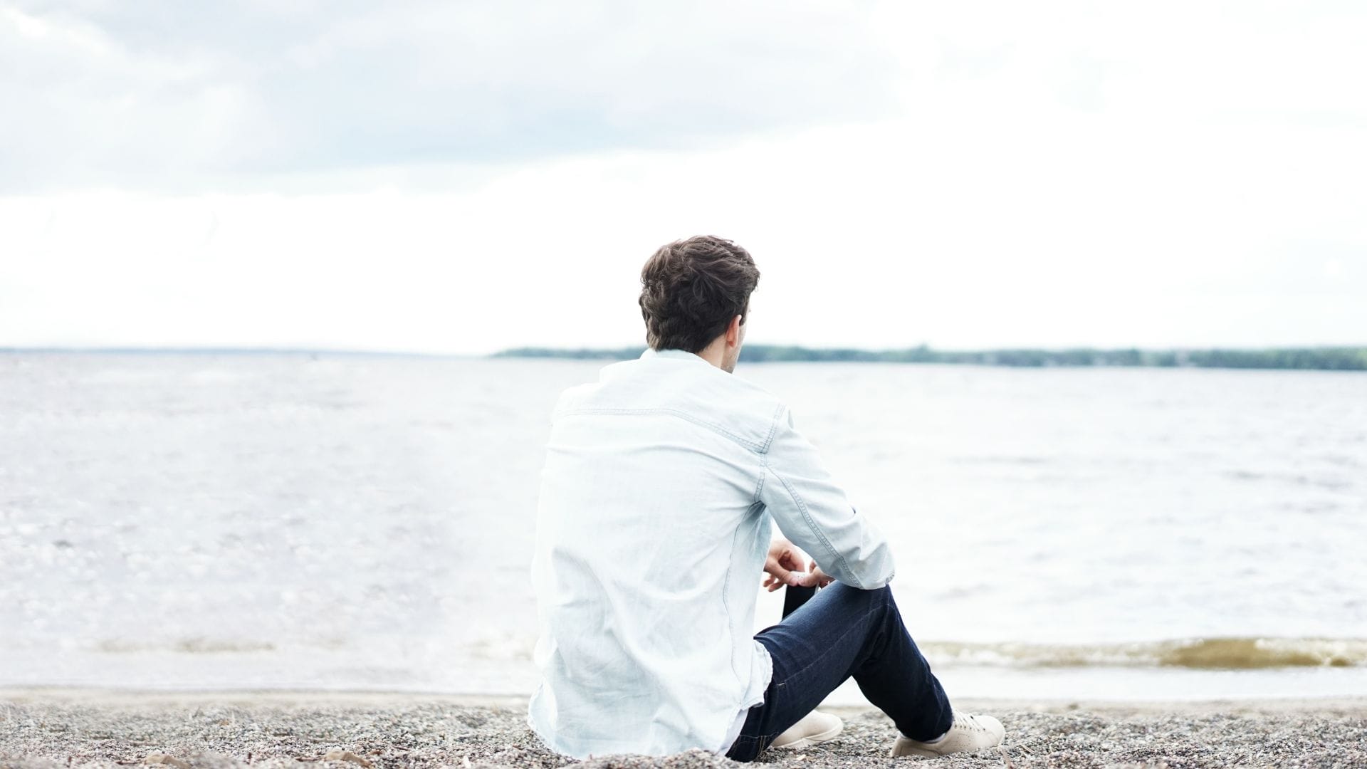 mann sitzt alleine am Wasser und schaut weg